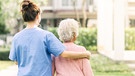 Rückenansicht einer Pflegekraft und einer älteren Frau in einem Garten.
| Bild: stock.adobe.com/interstid