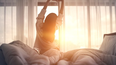 Eine junge Frau streckt sich früh morgens in Bett.  | Bild: stock.adobe.com/oatawa