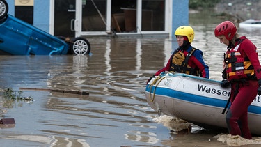 Mitarbeiterinnen der Wasserwacht ziehen am 01.06.2016 in Simbach am Inn (Landkreis Rottal-Inn) ein Schlauchboot durch das Hochwasser während im Hintergrund ein Auto kopfüber in den Fluten liegt. Nach anhaltendem Dauerregen ist ein Teil des Landkreises Rottal-Inn in Bayern am Mittwoch überschwemmt worden. Foto: Sven Hoppe/dpa | Bild: picture alliance / dpa | Sven Hoppe