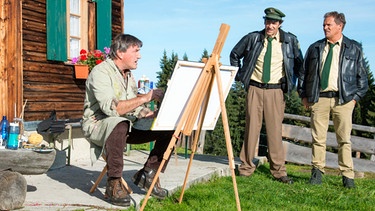 Hubert (Christian Tramitz, rechts) und Staller (Helmfried von Lüttichau, Mitte) sprechen mit dem Porträtmaler Herbert Stein (Johann Schuler). Der grantige Bayer war der beste Freund des Opfers und hatte noch am Tattag Besuch von Dr. Quirin Meyer auf seiner Hütte. | Bild: ARD/BR/TMG/Marco Meenen