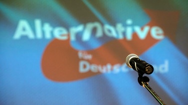 Ein Mikrofon steht beim Landesparteitag der der sächsischen AfD auf der Bühne vor dme Partei-Logo. | Bild: picture alliance/dpa | Sebastian Willnow