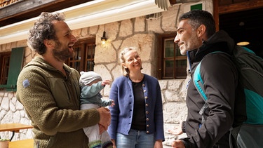 Die Reintalangerhütte im Wettersteingebirge: Moderator Marcus Fahn (rechts) auf der Terrasse mit den Hüttenwirtsleuten Andy und Julia Kechle und ihrem Sohn. | Bild: BR/Watch Lola GmbH/Matthias Schwinn