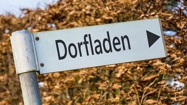 Ein Schild zeigt die Richtung zum Dorfladen. | Bild: stock.adobe.com/Thomas Reimer