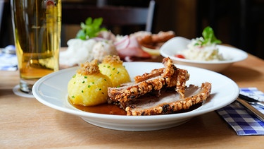 Ein Schweinebraten mit Kruste und Kartoffelknödel auf einem Teller. | Bild: stock.adobe.com/www.push2hit.de