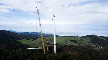 PRODUKTION - 17.10.2024, Baden-Württemberg, Freiburg: Ein Kran zieht das dritte Rotorblatt einer neuen Windkraftanlage auf der Holzschlägermatte am Schauinsland hoch. Die Anlage soll die dreifache Leistung der vorherigen Anlage liefern, die im Vorjahr nach 20 Betriebsjahren gesprengt wurde. Foto: Philipp von Ditfurth//dpa +++ dpa-Bildfunk +++ | Bild: dpa-Bildfunk/Philipp von Ditfurth