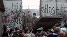 Ostdeutsche Grenzpolizisten blicken durch ein Loch in der Mauer | Bild: dapd