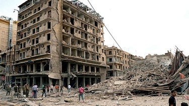 Syrische Polizisten und Bürger betrachten das von 3 Autobomben zerstörte BAB AMIR Hotel in Aleppo | Bild: picture-alliance/dpa