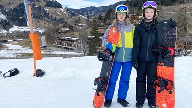 Zwei junge Mädchen stehen mit Snowboard im Schnee | Bild: BR | UNKRAUT