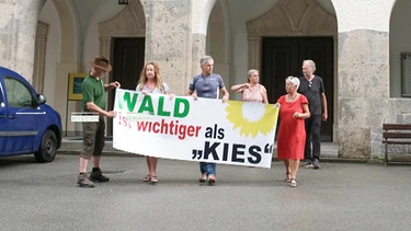 Foto einer Bürgerinitiative mit einem Plakat in der Hand mit der Aufschrift: Wald ist wichtiger als Kies. | Bild: BR