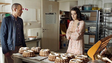 Cecilia Wittmann (Mona Vojacek Koper, r.) beteuert vor Jerry Paulsen (Peter Marton, l.), dass sie den Kuchen extra ohne Nuss zubereitet hat, da sie von Theresas starker Allergie wusste. | Bild: ARD/Lucky Bird Pictures/Savoy Film Productions