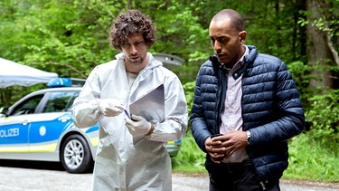 Ein Tatort am Holzlagerplatz: Der Tote ist Kabarettist Kuno Horn. Dr. Philipp Hartmann (Jakob Graf, l.) klärt Jerry (Peter Marton, r.) über die Umstände auf. | Bild: ARD / Billy Gropper