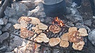 Kleine Brotfladen liegen auf einem Rost über einem Lagerfeuer. | Bild: Rainer Schall