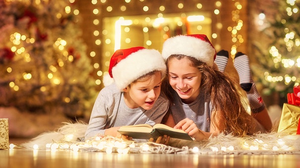 Zwei Kinder lesen vor einem Weihnachtsbaum ein Buch | Bild: Colourbox