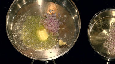 Von oben fotografiert: zwei Knoblauchzehen in einem Topf mit geschnittenen Zwiebeln | Bild: Wir in Bayerno