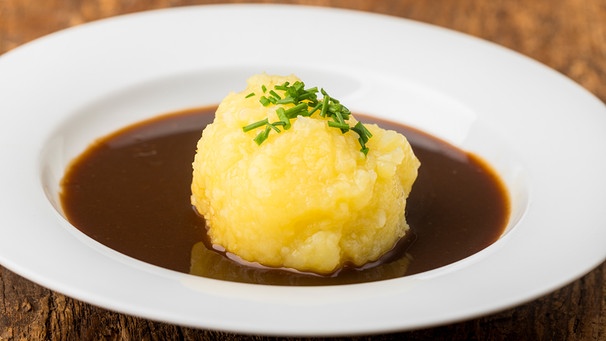 ein Kartoffelknödel mit dunkler Bratensoße in einem weißen Teller | Bild: mauritius images / Bernd Jürgens