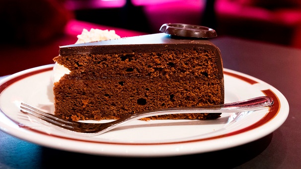 ein Stück Sachertorte auf einem weißen kleinen Teller mit einer Kuchengabel | Bild: 	mauritius images / Irina Naoumova / Alamy / Alamy Stock Photos