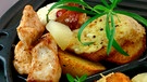 Ein Raclette-Pfännchen gefüllt mit Hühnchenbruststücken, Kartoffeln, die mit Käse überbacken sind, einem Stück Ananas, gebratenem Speck und etwas Rosmarinstängel | Bild: mauritius images / Pitopia / Liz Collet