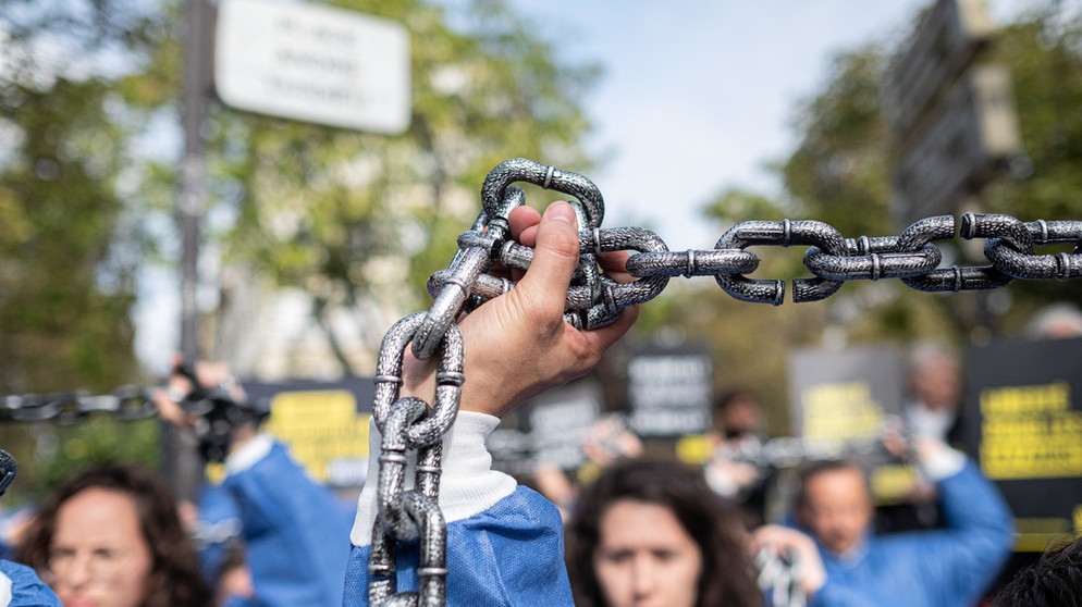 Paris: Demonstranten tragen blaue Anzüge und tragen Ketten während Sie an einer von Amnesty International organisierten Demonstration teilnehmen, um mutmaßliche Menschenrechtsverletzungen gegen die uigurische Minderheit in China anzuprangern. | Bild: dpa-Bildfunk/Olivier Donnars