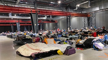 Messehalle in Warschau, allein einer Halle müssen 1000 Menschen auf Liegen schlafen und hoffen, dass sie irgendwie weiterkommen. | Bild: BR/WDR/Isabel Schayani