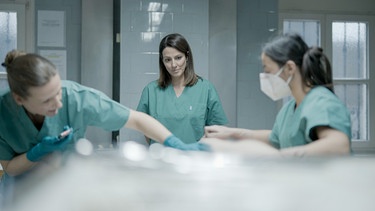 Im Obduktionssaal von Gerichtsmedizinerin Sarah Heinze (links) sieht Lisa Gadenstätter (Mitte) zum ersten Mal eine Leiche. | Bild: ORF/BFilm