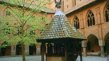 Ein Innenhof der Burganlage von Burg Malbork mit gotischen Stilelementen an Fassade und Brunnen. | Bild: BR/SWR