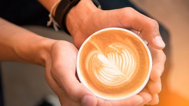 Mann hält Tasse mit Capuccino mit Hafermilch | Bild: mauritius images