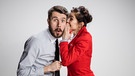 Eine Frau flüstert einem Mann etwas ins Ohr, der entsetzt und belustigt zugleich schaut. | Bild: colourbox.com
