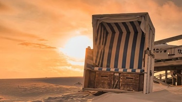 Ein Strandkorb steht in der Abendsonne neben einer Seebrücke | Bild: NDR