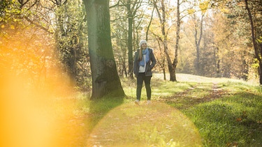 Eine Frau geht in einem herbstlichen Wald spazieren. | Bild: picture alliance / dpa-tmn / Christin Klose