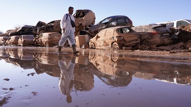 Mann geht an aufgestapelten Autos vorbei, nachdem die Überschwemmungen in Catarroja in der Region Valencia in Spanien Verwüstungen und Hunderte von Toten und Vermissten hinterlassen haben. | Bild: dpa-Bildfunk/Alberto Saiz