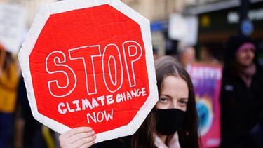 06.11.2021, Großbritannien, Glasgow: Eine Demonstrantin hält ein Plakat in der Form eines Stoppschildes nach oben, auf dem zu lesen ist «Stoppt den Klimawandel Jetzt» (Stop Climate Change Now).  | Bild: dpa-Bildfunk/Ben Birchall