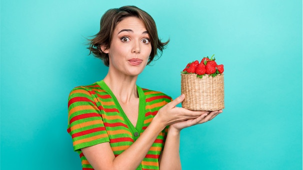 Eine Frau hält einen Korb mit Erdbeeren in der Hand, leckt die Lippen. Wie gesund sind Erdbeeren, wie wascht ihr sie richtig? Und ist die Erdbeere eine Nuss oder eine Frucht? Hier erfahrt ihr spannende Fakten über das rote Lieblingsobst. | Bild: Wochit/Getty Images