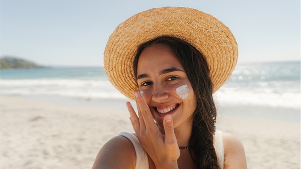 Eine junge Frau am Strand cremt sich mit Sonnencreme ein. Immer mehr Menschen in Deutschland erkranken an Hautkrebs. Deshalb ist ein guter Sonnenschutz vor der Sonne und UV-Strahlung wichtig. Wir erklären euch, was ihr beachten müsst. | Bild: Wochit/Getty Images