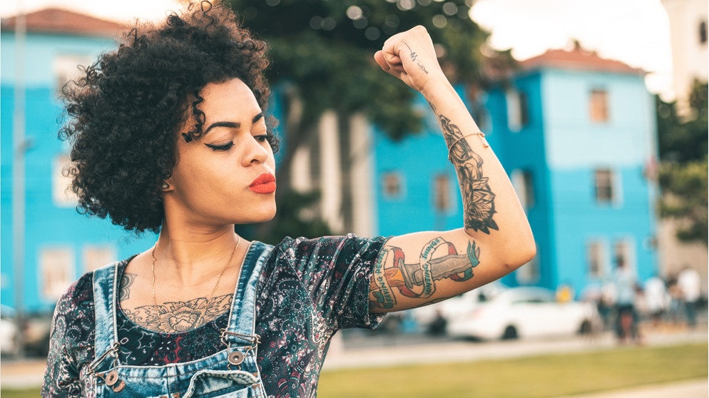 Eine Frau mit Tattoos hebt den Arm und spannt die Muskeln an.  | Bild: Wochit/Getty Images