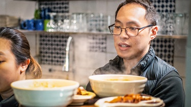 Ein Mann steht in seiner Küche vor mehreren dampfenden Schüsseln mit Essen. | Bild: hr/isar film Produktion GmbH