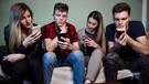 Vier junge Erwachsene schauen in ihre Smartphones. | Bild: stock.adobe.com/phoenix021