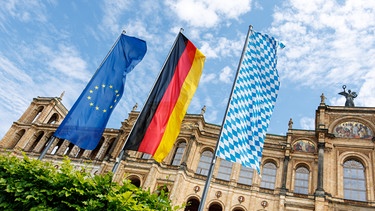 (Archivbild) Die europäische, die deutsche und die bayerische Flagge wehen vor dem Maximilianeum, Sitz des Bayerischen Landtags. | Bild: picture alliance/dpa/Matthias Balk