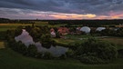 Der Möhrendorfer Ortsteil Oberndorf bei Sonnenuntergang. Auf der einen Seite spiegeln sich die Wolken im Weiher auf der anderen Seite ragt eine Biogasanlage in die Höhe. | Bild: Björn Hutzler, Möhrendorf, 07.07.2024