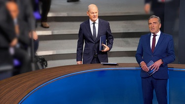 BR24-Moderator Stefan Scheider neben einem Bild von Olaf Scholz | Bild: Bayerischer Rundfunk 2024