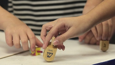 Kinder spielen mit einem Chanukka-Dreidel, einer Art Kreisel. Chanukka ist ein jüdisches Lichterfest, das in manchen Bräuchen an Weihnachten erinnert. | Bild: picture alliance | AP Images