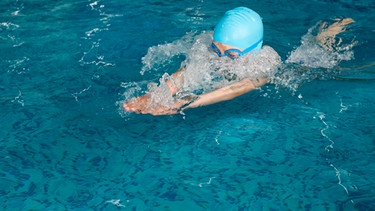 Eine Mädchen mit Schwimmkappe und Schwimmbrille im Wasser eines Schwimmbads. | Bild: colourbox.com