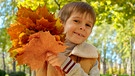 Ein kleiner Junge mit einem Bündel bunter Herbstblätter in den Händen. | Bild: colourbox.com