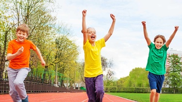 Drei Kinder jubeln beim Laufen auf einer Tartanbahn. | Bild: colourbox.com