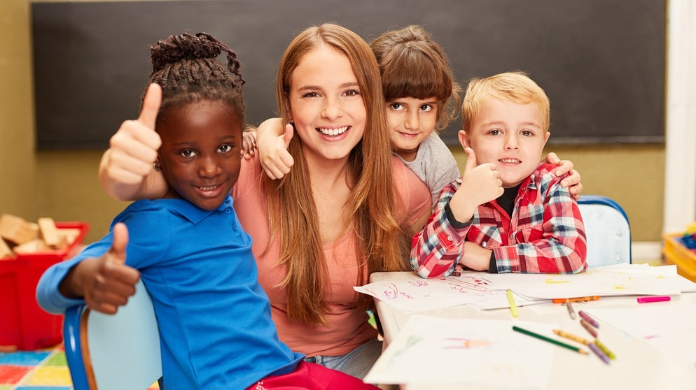 Fröhliche Schulkinder umringen eine Frau und recken alle den Daumen in die Höhe. | Bild: picture alliance / Zoonar | Robert Kneschke