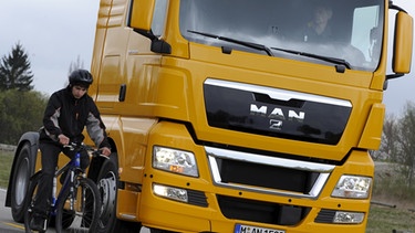 Ein Fahrradfahrer steht während einer Pressevorführung auf einer LKW-Teststrecke bei München (Oberbayern) im toten Winkel eines LKWs.  | Bild: picture-alliance/dpa