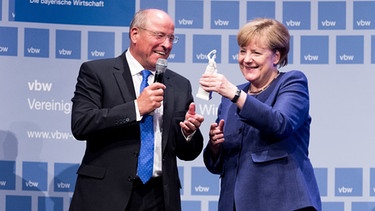 Alfred Gaffal (l), der Präsident der Vereinigung der Bayerischen Wirtschaft, überreicht Bundeskanzlerin Angela Merkel (CDU) am 11.07.2017 in München (Bayern) eine kleine Bavaria-Statue. Merkel spricht beim 39. Bayerischen Wirtschaftsgespräch über aktuelle politische Herausforderungen. | Bild: pa/dpa/Alexander Heinl