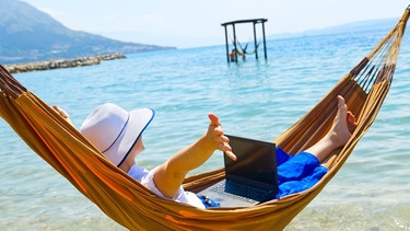 junge Frau mit Laptop in Hängematte am Meer | Bild: picture alliance / Zoonar | Ilja Enger-Tsizikov