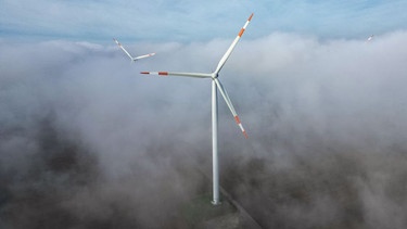 ARCHIV - 18.10.2023, Sachsen-Anhalt, Querfurt: Die Windräder in einem Windpark ragen aus dem Morgennebel hervor. Kommunen sollen unbürokratischer am Ausbau von erneuerbaren Energien beteiligt werden. (Luftaufnahme mit Drohne) (zu dpa: «Kommunen sollen am Ausbau von Erneuerbaren beteiligt werden») Foto: Jan Woitas/dpa +++ dpa-Bildfunk +++ | Bild: dpa-Bildfunk/Jan Woitas