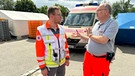 Pfarrer Klaus Kuhn (rechts) im Gespräch mit einem Helfer des Deutschen Roten Kreuzes. | Bild: BR / Martin Jarde