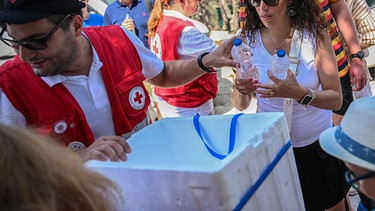 Mitarbeiter des Roten Kreuzes verteilen Wasserflaschen an Touristen (Symbolbild) | Bild: picture-alliance/dpa | Angelos Tzortzinis